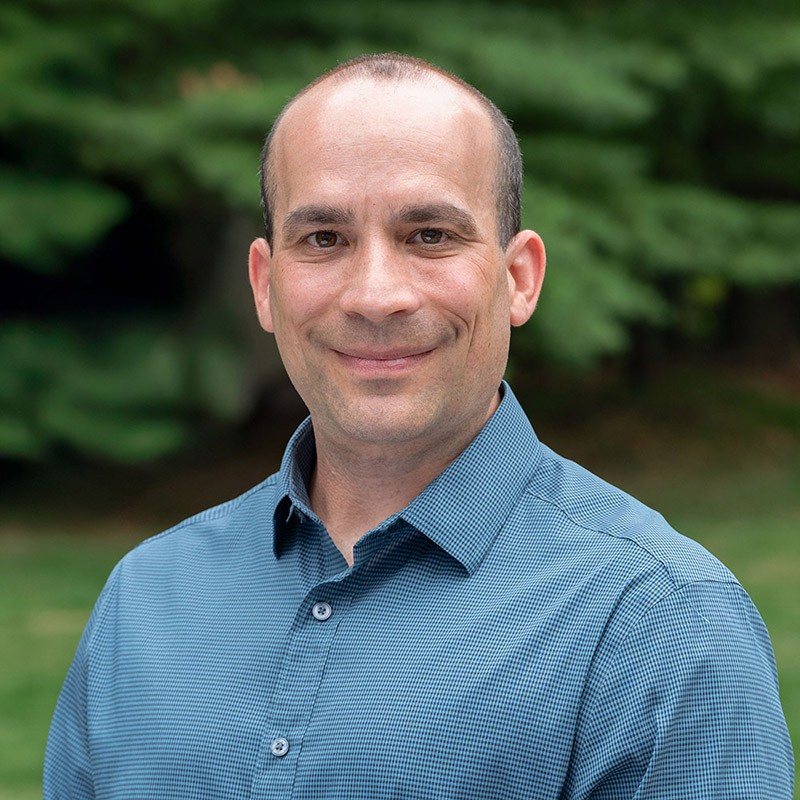Seth Lutsky smiling outdoors in a blue checked shirt.