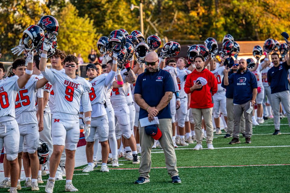 Manalapan varsity players raise their helmets together on the field.
