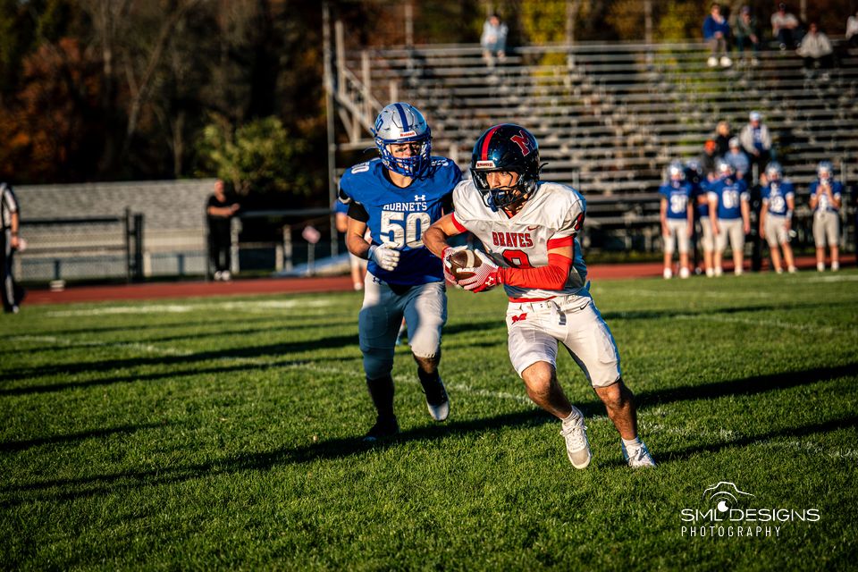 A Manalapan ball carrier in white tucks the ball and cuts past a defender in blue.