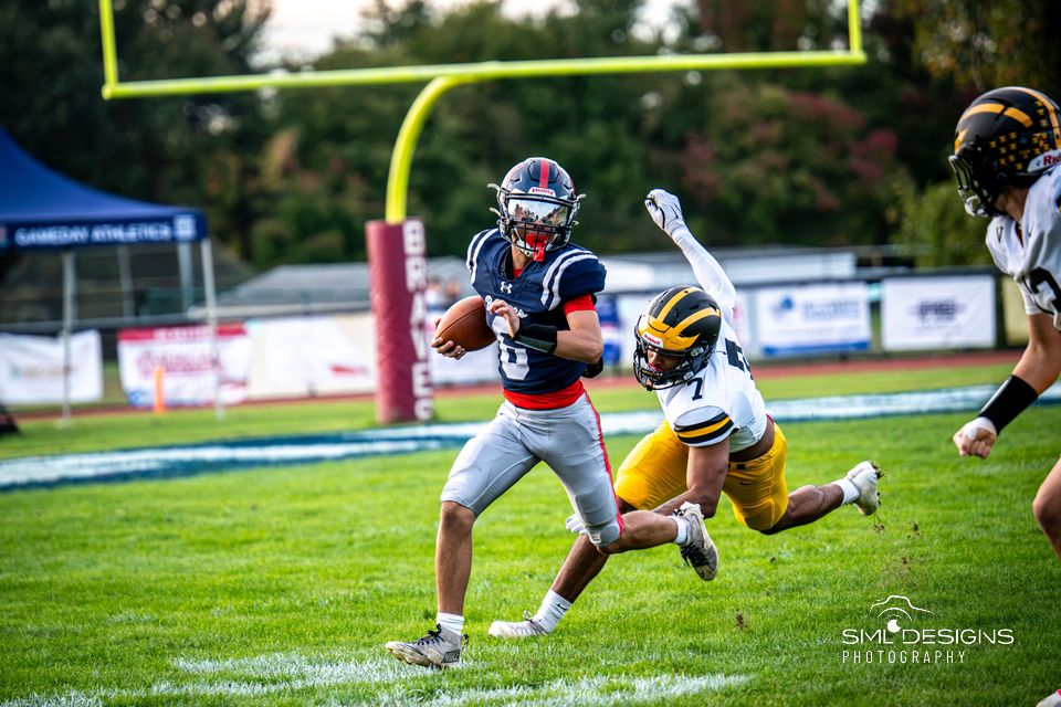 A Manalapan ball carrier in navy breaks away as a defender in gold dives at his feet.